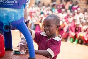 A pupil from Exodus Academy pours a glass of safe water from the new LifeStraw Community purifier, replacing dirty water from a local stream