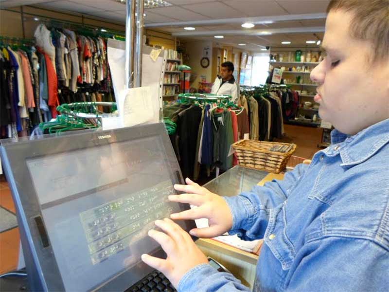 Volunteer Harry uses the braille till overlay at a WESC Foundation shop